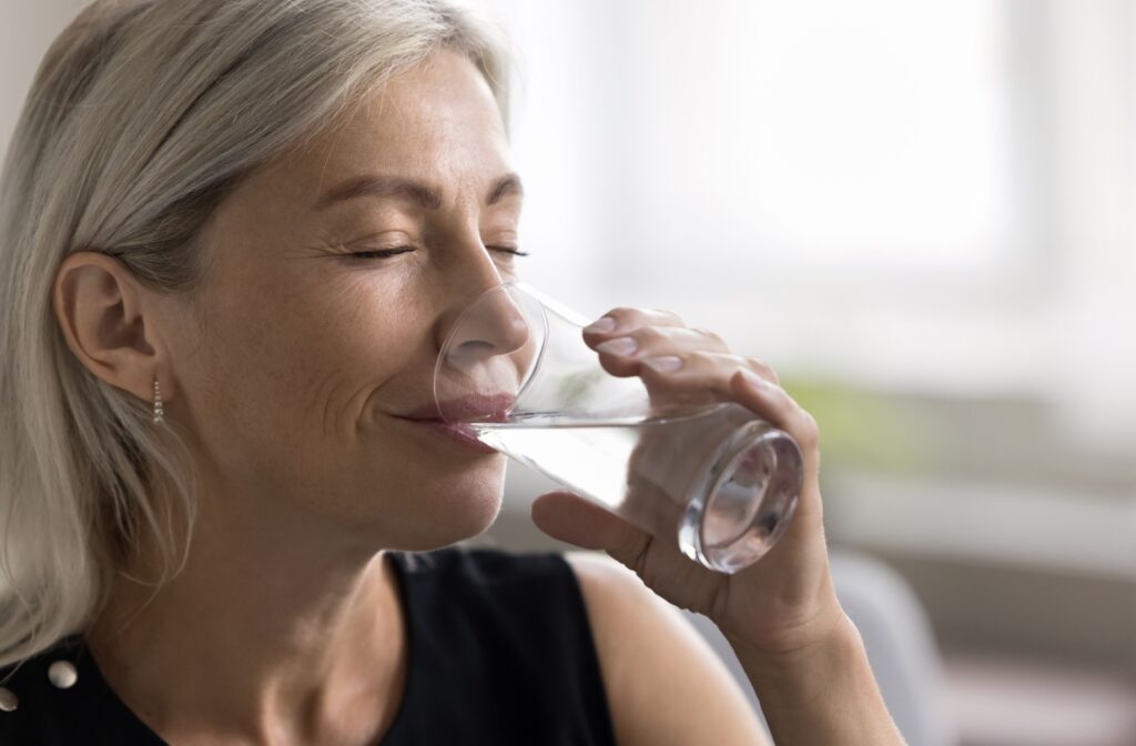 Mature woman in a black top drinking fluoridated tap water to support cavity prevention and oral health benefits.