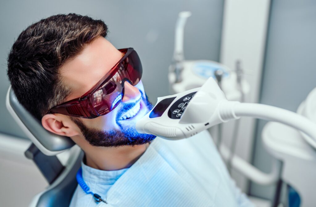 An adult staying still in their dentist's chair while getting a laser whitening treatment.