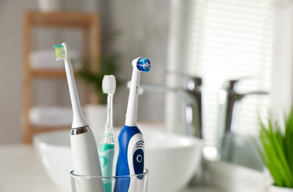 A cup holding three different toothbrushes, two of which are electric toothbrushes and one which is a manual toothbrush.