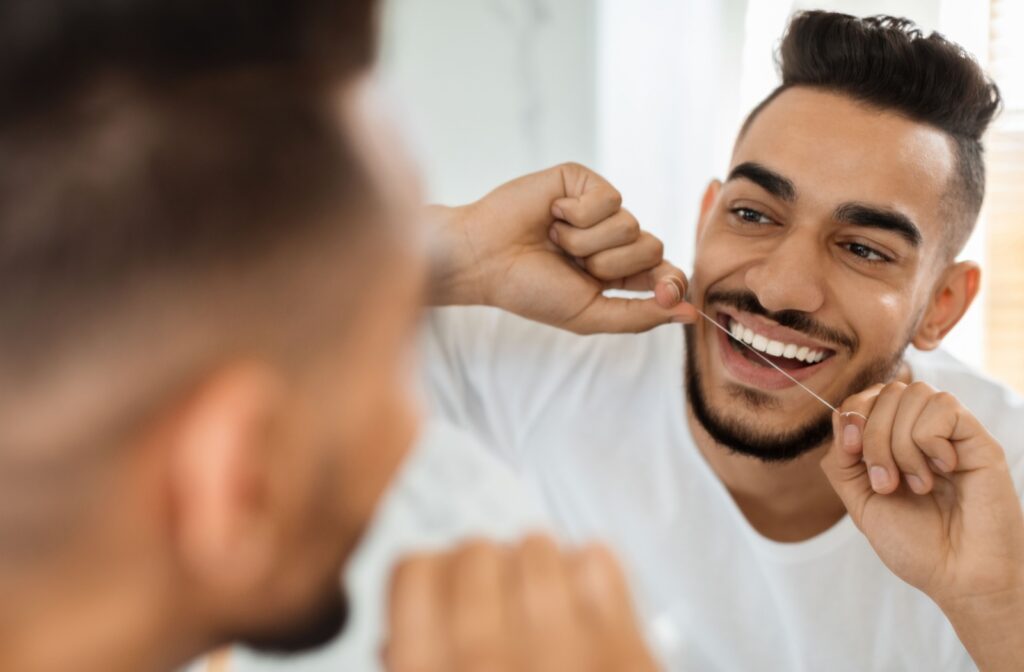 A person looking in the mirror smiling as they floss in between their teeth